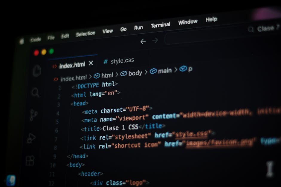 A person with light skin is using a laptop with a black keyboard and a thin silver frame, placed on a dark, reflective surface. The laptop screen displays lines of colorful code in a dark-themed text 